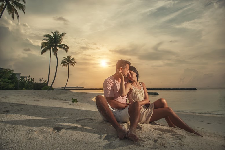 Couple holding each other while sitting on the beach at sunset